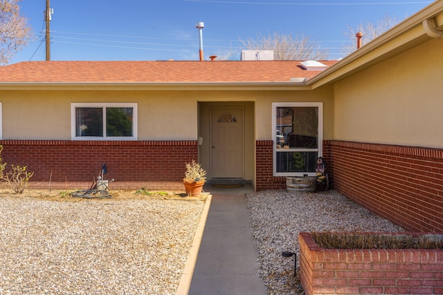 property entrance featuring brick siding, roof with shingles, and stucco siding