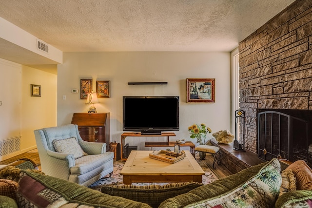 living room with visible vents, a fireplace, a textured ceiling, and wood finished floors