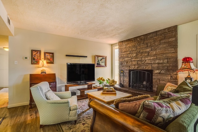 living room featuring a stone fireplace, a textured ceiling, baseboards, and wood finished floors