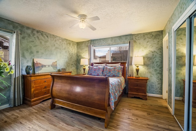 bedroom featuring a ceiling fan, a textured ceiling, wood finished floors, wallpapered walls, and baseboards