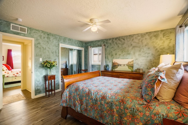 bedroom featuring visible vents, a textured ceiling, wood finished floors, and wallpapered walls