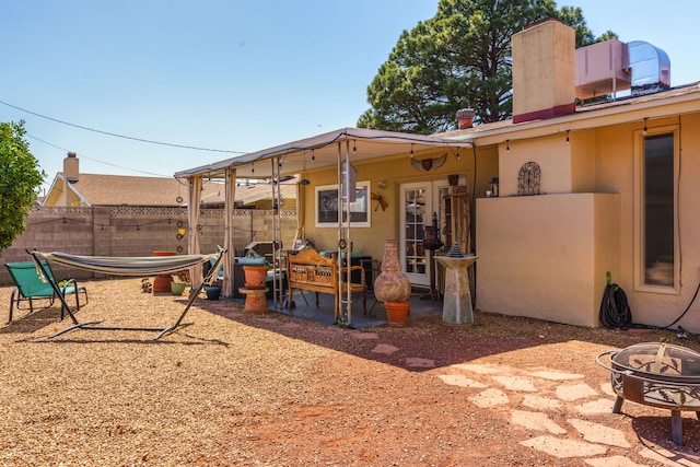 rear view of house featuring stucco siding, a patio, fence, a fire pit, and a chimney