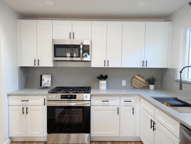 kitchen featuring white cabinets, appliances with stainless steel finishes, light countertops, and a sink