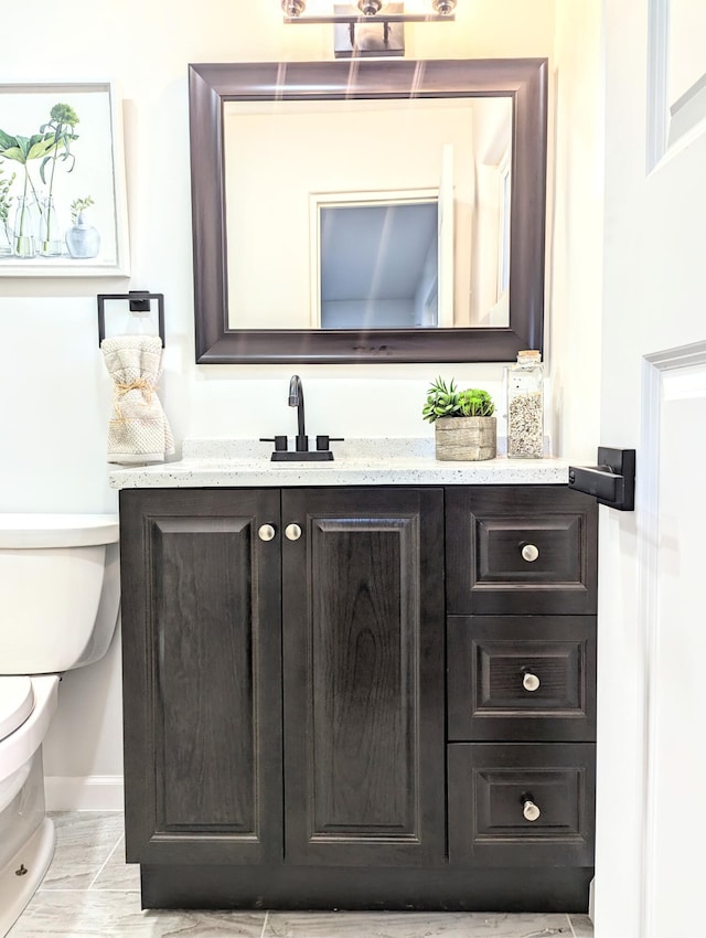 half bathroom with baseboards, toilet, and vanity