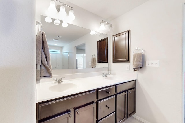 full bathroom with double vanity, a shower stall, baseboards, and a sink