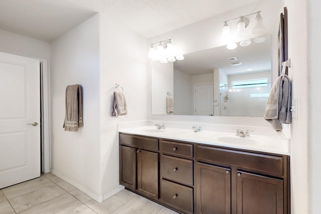 full bathroom with a shower stall, double vanity, baseboards, and a sink