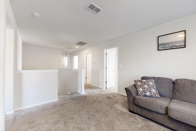 living area featuring baseboards, visible vents, a textured ceiling, and carpet