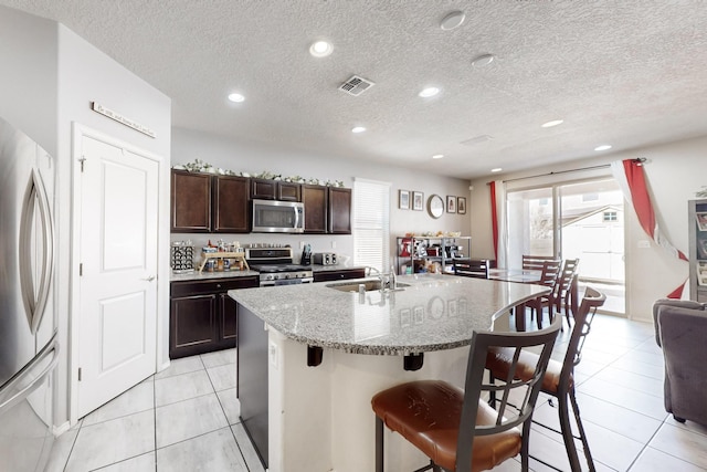 kitchen with a breakfast bar area, visible vents, a kitchen island with sink, a sink, and appliances with stainless steel finishes