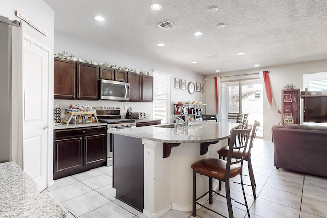 kitchen with visible vents, light stone countertops, a breakfast bar area, appliances with stainless steel finishes, and a sink