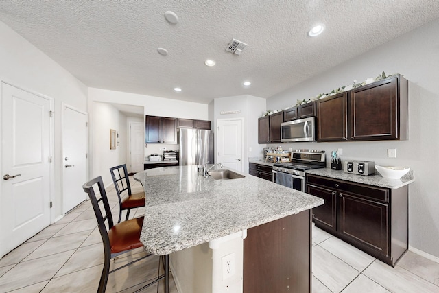 kitchen featuring visible vents, a breakfast bar, a sink, stainless steel appliances, and dark brown cabinets