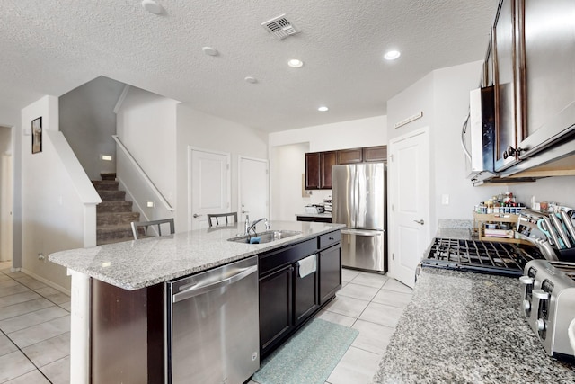 kitchen with light stone countertops, visible vents, an island with sink, a sink, and appliances with stainless steel finishes