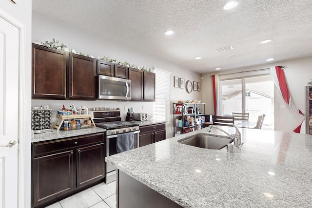 kitchen with dark brown cabinets, light stone countertops, light tile patterned floors, appliances with stainless steel finishes, and a sink