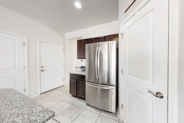 kitchen featuring light tile patterned floors, freestanding refrigerator, light countertops, dark brown cabinetry, and a textured ceiling