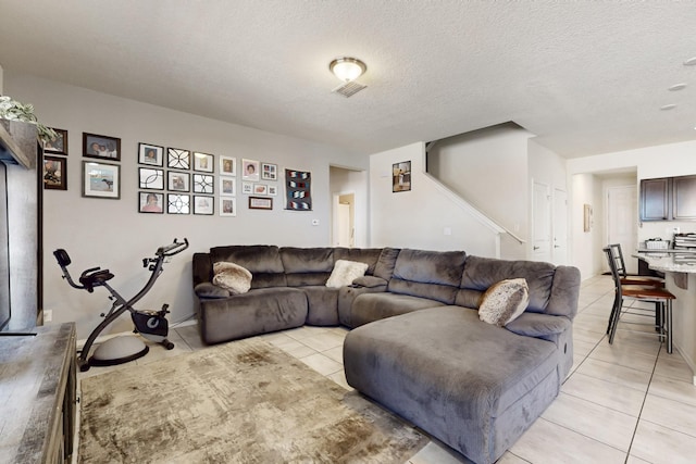 living area with light tile patterned flooring, visible vents, a textured ceiling, and stairs