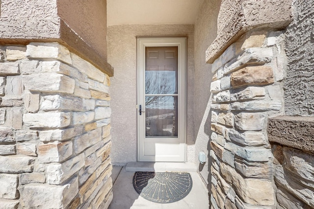 view of exterior entry featuring stucco siding and stone siding