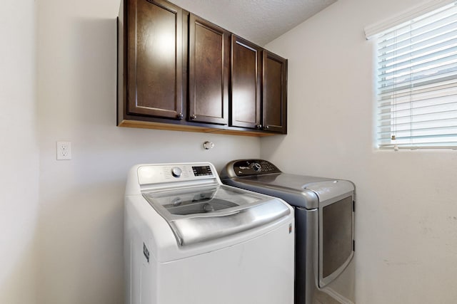 clothes washing area with cabinet space, a textured ceiling, a healthy amount of sunlight, and washing machine and dryer