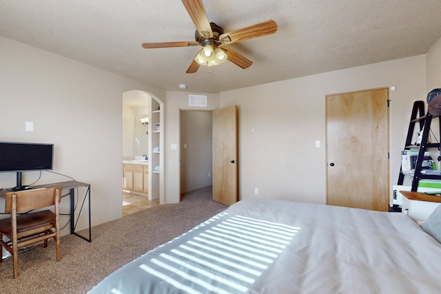 bedroom featuring carpet floors, arched walkways, visible vents, connected bathroom, and a textured ceiling