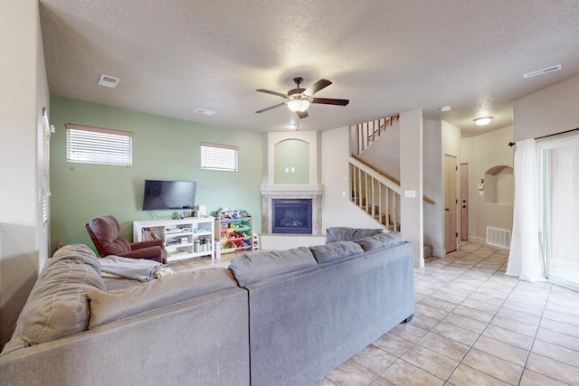 living room featuring a glass covered fireplace, visible vents, stairway, and a textured ceiling