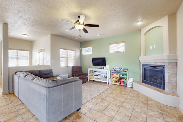 tiled living area with a ceiling fan, a fireplace, plenty of natural light, and visible vents