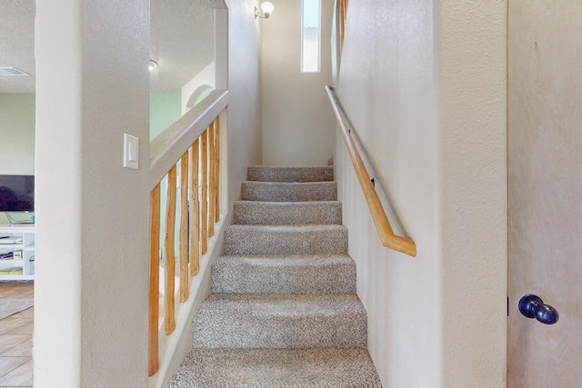 staircase with visible vents, a textured ceiling, and a textured wall