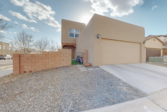 pueblo-style home featuring a gate, driveway, an attached garage, and stucco siding