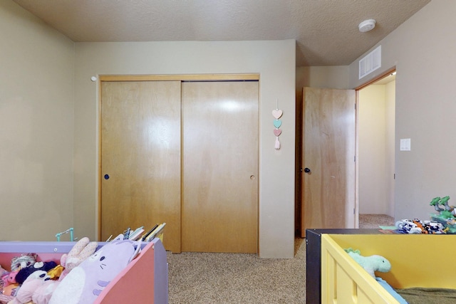 bedroom with light carpet, a textured ceiling, visible vents, and a closet