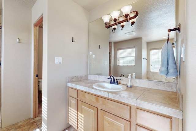 bathroom featuring a textured ceiling, toilet, vanity, and visible vents