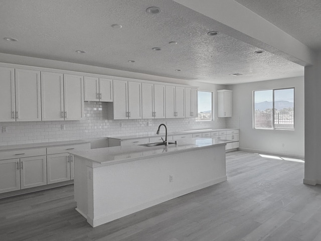 3340 Wolf Tail Loop NE, Rio Rancho, NM 87144 - kitchen with a textured ceiling, backsplash, white cabinetry, light wood-style floors, and a center island with sink