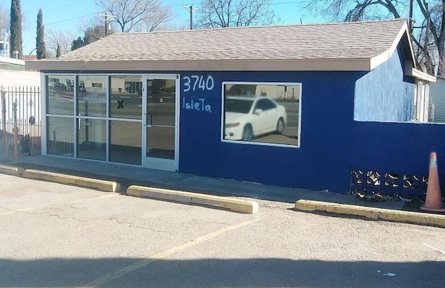 exterior space featuring uncovered parking, a shingled roof, and fence