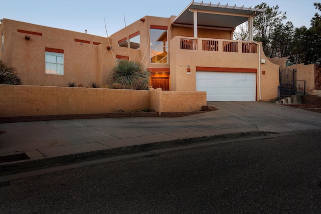 pueblo-style home with driveway, a balcony, an attached garage, a gate, and stucco siding