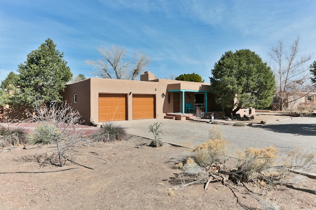 pueblo revival-style home with stucco siding, a garage, a chimney, and driveway