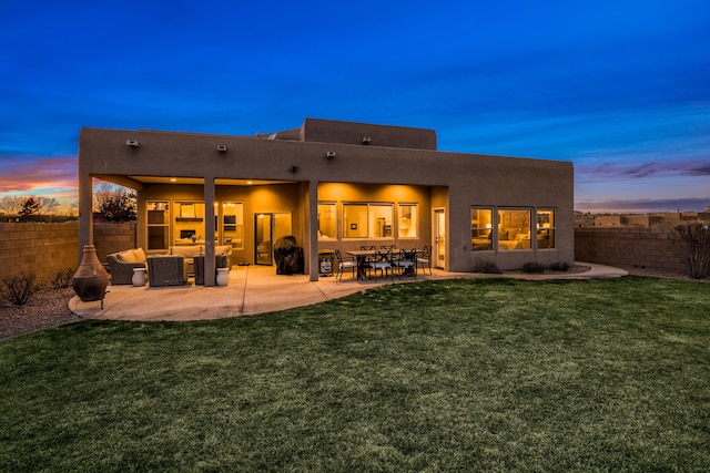 back of house at dusk featuring a patio area, a fenced backyard, a yard, and stucco siding