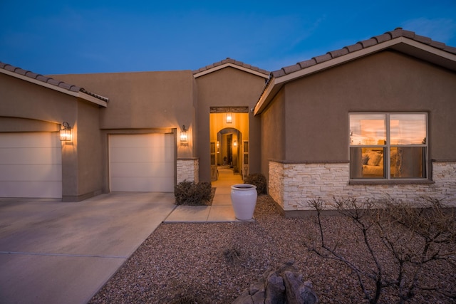 view of front facade with stone siding, driveway, an attached garage, and stucco siding