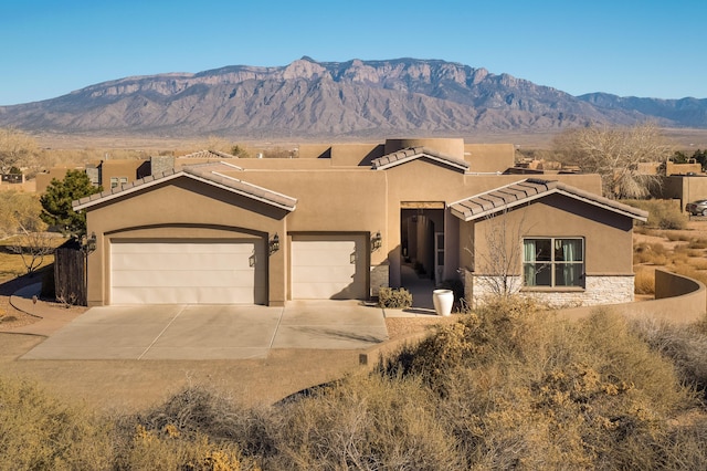 view of front facade with stone siding, concrete driveway, a mountain view, and stucco siding