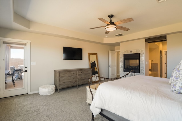 bedroom featuring carpet, a ceiling fan, baseboards, a tray ceiling, and a tiled fireplace