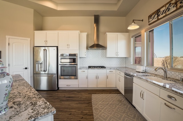 kitchen with a sink, light stone countertops, stainless steel appliances, wall chimney range hood, and backsplash