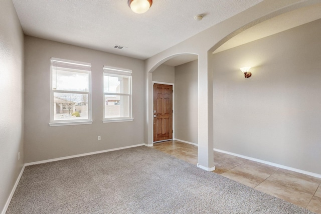 empty room featuring visible vents, light carpet, a textured ceiling, arched walkways, and baseboards