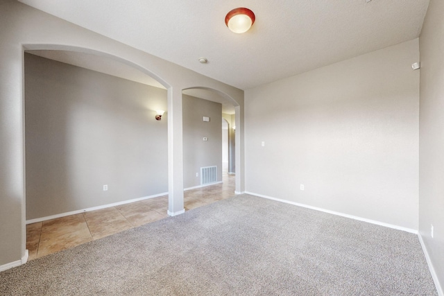 empty room featuring visible vents, baseboards, light carpet, light tile patterned floors, and arched walkways