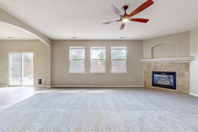 unfurnished living room featuring a fireplace, carpet, arched walkways, and a textured ceiling