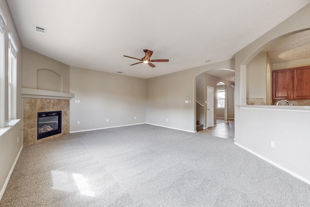 unfurnished living room featuring visible vents, carpet floors, a fireplace, arched walkways, and a ceiling fan