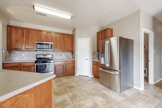 kitchen with visible vents, appliances with stainless steel finishes, light tile patterned flooring, brown cabinetry, and light countertops