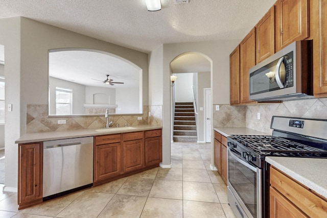 kitchen featuring brown cabinets, a sink, stainless steel appliances, arched walkways, and light countertops