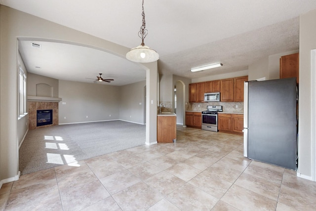 kitchen featuring brown cabinetry, light countertops, arched walkways, stainless steel appliances, and a ceiling fan