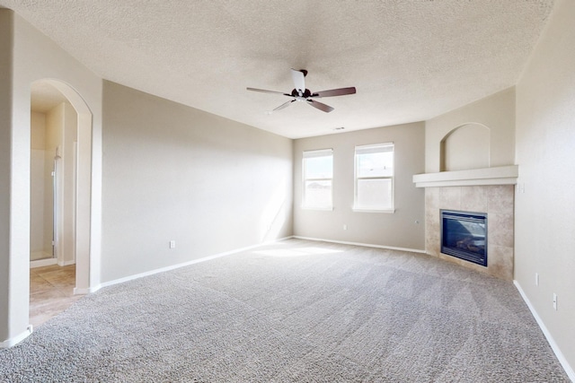 unfurnished living room featuring ceiling fan, baseboards, a tiled fireplace, carpet, and a textured ceiling