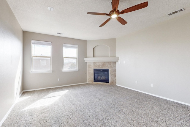 unfurnished living room with visible vents, ceiling fan, carpet floors, a tile fireplace, and a textured ceiling