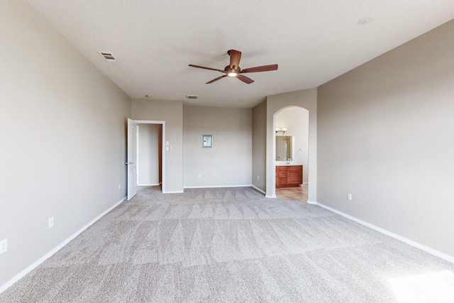 unfurnished bedroom with visible vents, connected bathroom, arched walkways, baseboards, and light colored carpet