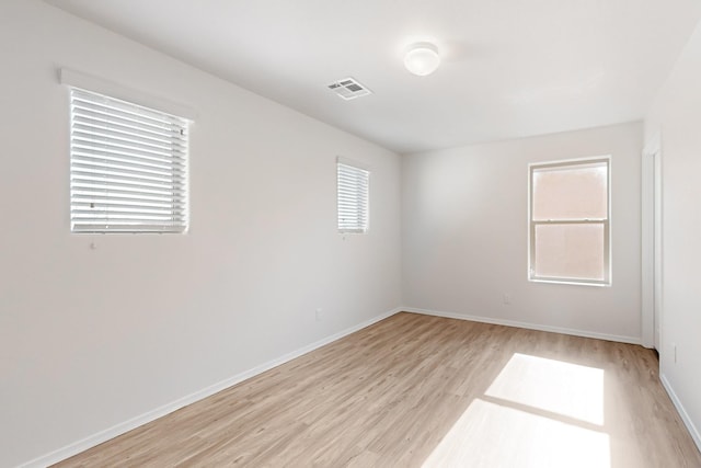 spare room featuring light wood-type flooring, visible vents, and baseboards