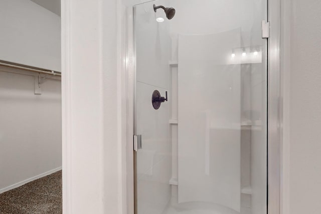 bathroom featuring a shower stall, a walk in closet, and baseboards