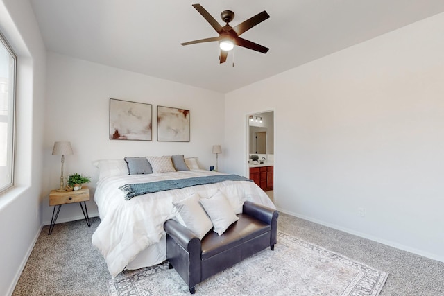 bedroom featuring connected bathroom, baseboards, light colored carpet, and ceiling fan