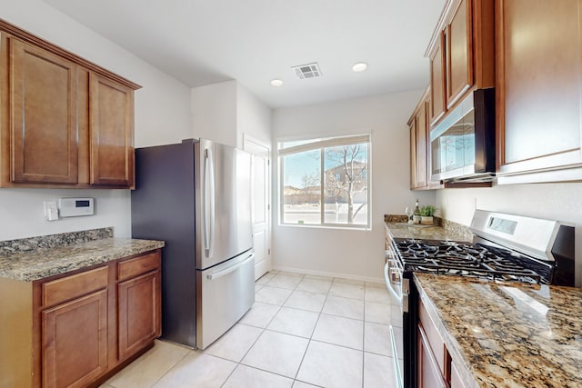 kitchen featuring appliances with stainless steel finishes, light tile patterned flooring, brown cabinetry, baseboards, and light stone countertops